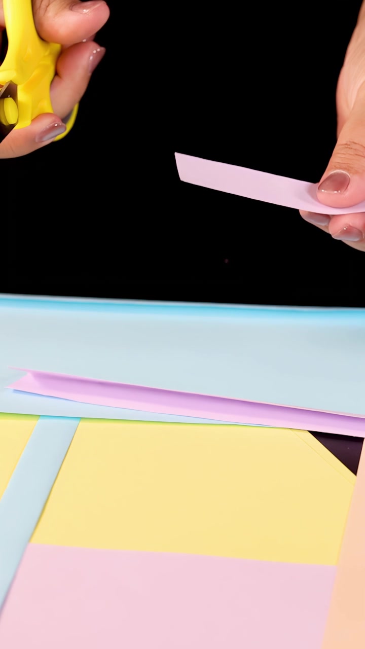 Mani tagliano strisce di carta pastello con le forbici su uno sfondo nero sotto una luminosa illuminazione da studio