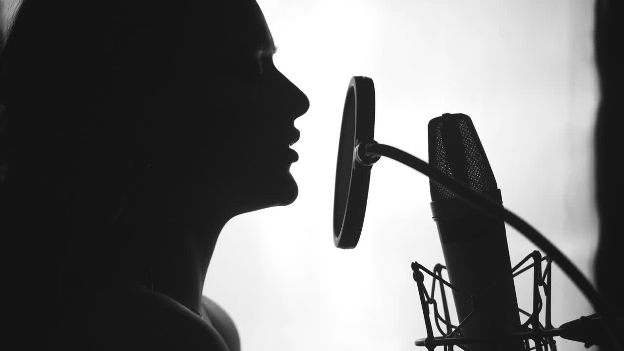 Young sexy profile of a woman with a beautiful face and lips. Girl singing to the microphone in a studio. Black and white