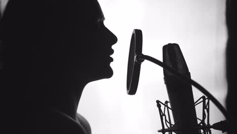 young sexy profile of a woman with a beautiful face and lips. girl singing to the microphone in a studio. black and white
