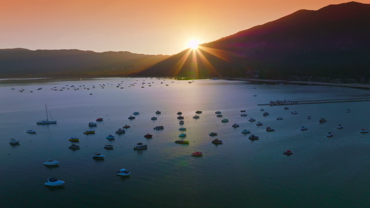 Yachts and boats holding still on the waters of Lake Tahoe, California, USA. Dark mountains silhouettes with setting sun at backdrop.