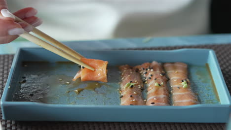 A-woman-with-chopsticks-in-hand-takes-thin-slices-of-salmon-marinated-at-restaurant,-shot-at-30-fps