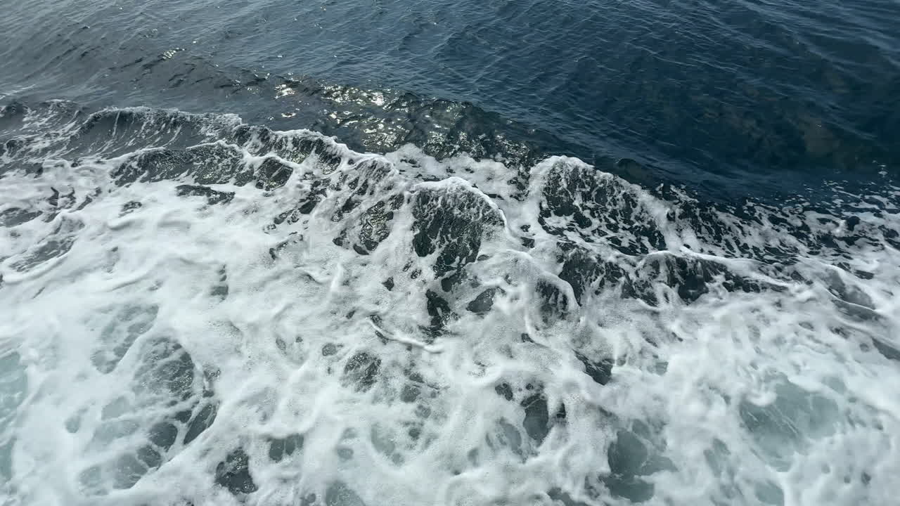 Foamy waves created by a boat wake splash across the deep blue sea, capturing the power, energy, and motion of the ocean surface