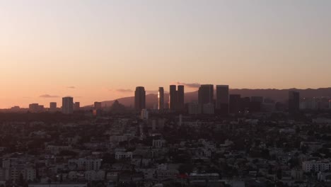 Drone-rising-fast-revealing-Los-Angeles-Skyline-during-Sunset,-Warm-colors-sky,-California