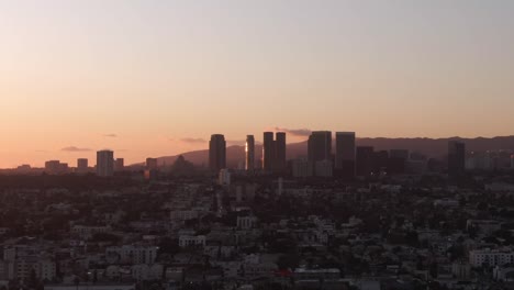 Drone-Subiendo-Rápidamente-Revelando-El-Horizonte-De-Los-Angeles-Durante-La-Puesta-De-Sol,-Cielo-De-Colores-Cálidos,-California