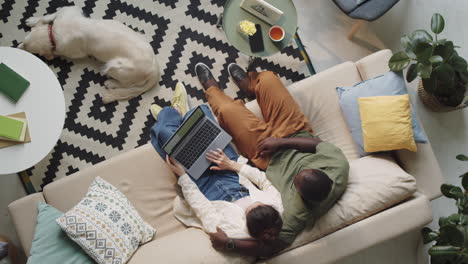 family couple using laptop and speaking on sofa at home