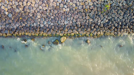 aerial of small waves from the lake hit the stone shore line, top down.