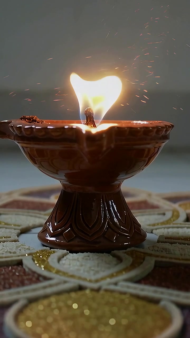 Vertical video: Zooming clay diya flame elongating, wick sending embers on glitter mat