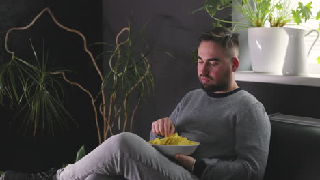 hungry man sitting on sofa and eating delicious potato chips