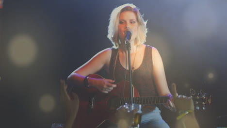 female musician performing music on stage playing acoustic guitar and singing, showing bokeh lights