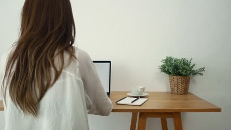 beautiful young smiling woman working on laptop while enjoying drinking warm coffee sitting in a living room at home. enjoying time at home. asian business woman working in her home office.