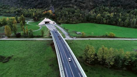 aerial view with a drone over highway roads going into a tunnel in france. only grass fields and trees around the roads. cars and trucks driving on the roads.