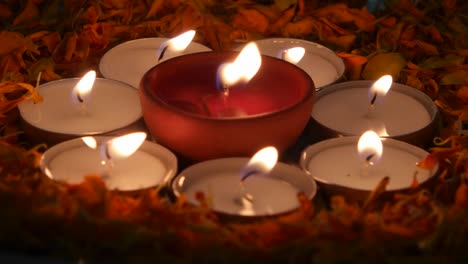 pan to close up of diyas or indian earthen lamp in a silver plate with marigold petals, lit up for diwali 'festival of light',surrounded by lit tea-light candles