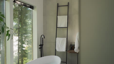 stylish bathroom and couple brushing teeth. bathtub and ladder rack by panoramic window in hotel room. guests of luxury resort do morning routine