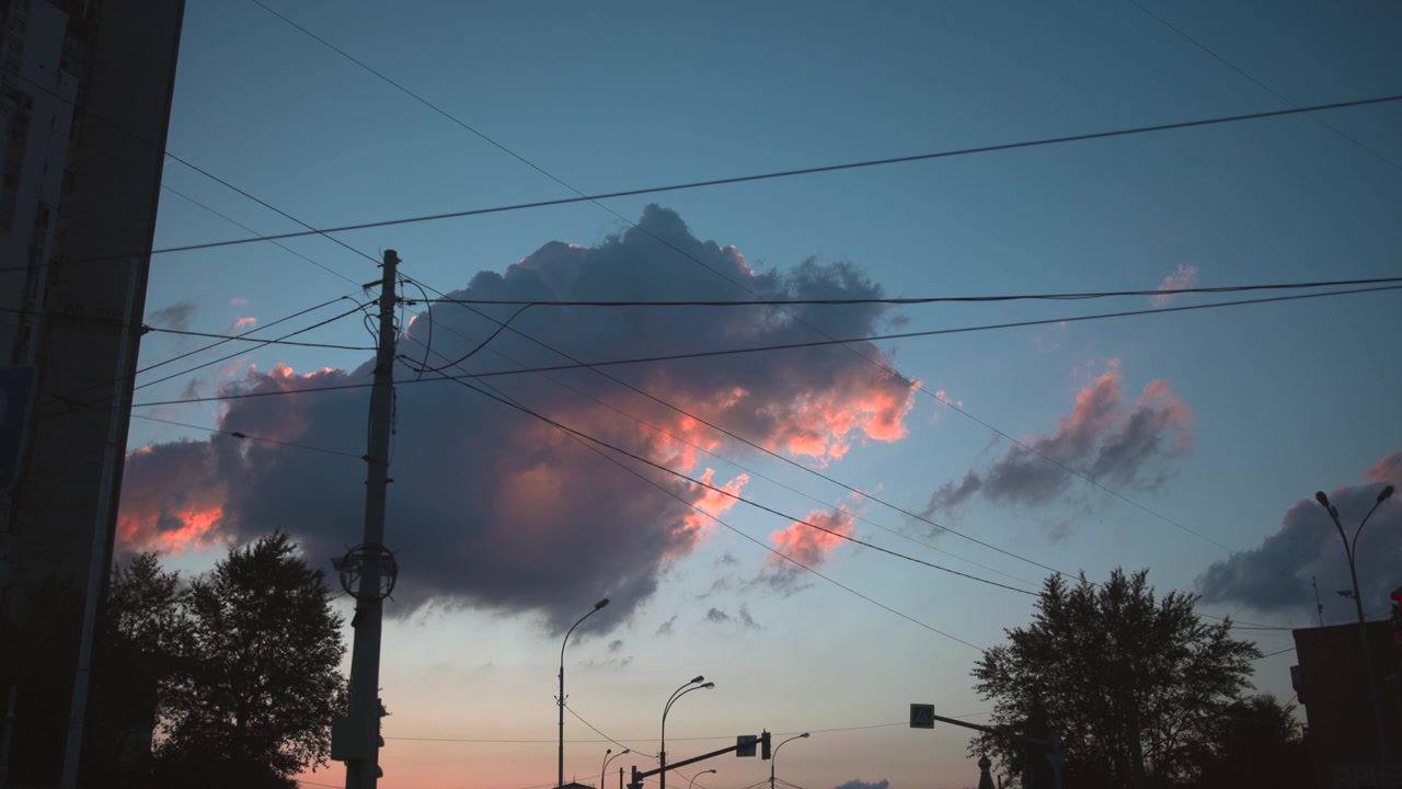 serene evening sky with clouds over urban environment at dusk, featuring power lines, buildings, and trees from a window or high vantage point, creating a peaceful and calm atmosphere.