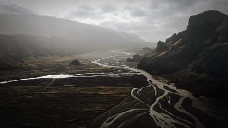 dramatic aerial thor valley, glacial river flowing through black volcanic mountain, thorsmörk cinematic moody iceland