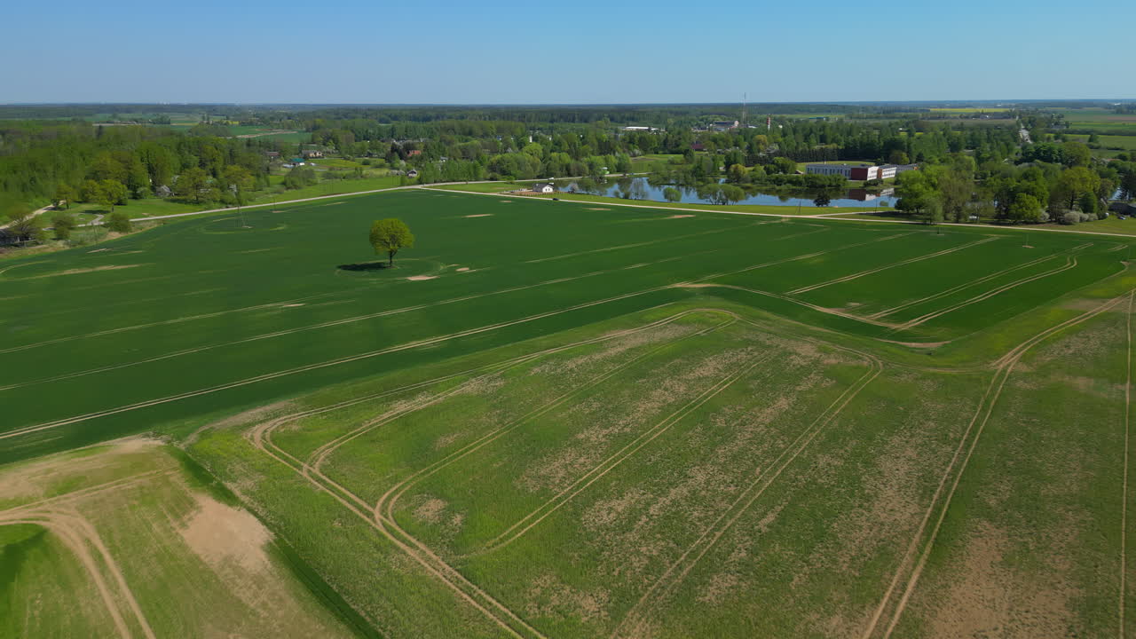 drone volando sobre una comunidad agrícola, tierra abierta, pequeño lago, y varias casas y edificios en el fondo