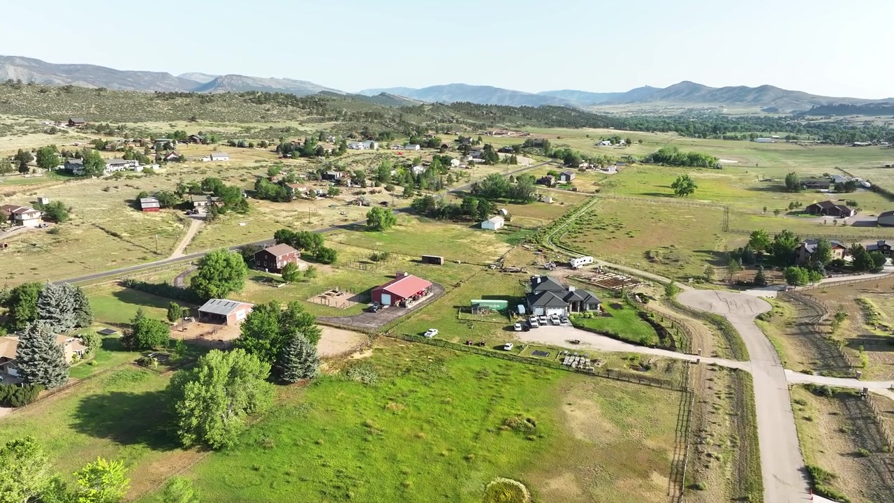 Toma de dron en ángulo alto mostrando casas rurales y extensas propiedades verdes ubicadas al pie de las estribaciones rocosas de Loveland, Colorado
