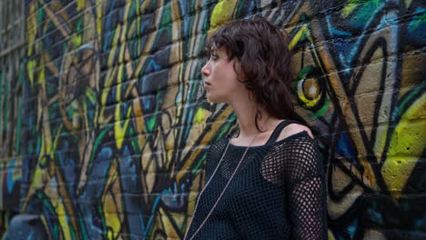retrato de moda al aire libre de una mujer joven de estilo alternativo apoyándose en una pared cubierta de graffiti en la calle city street de londres, reino unido, en tiempo real.