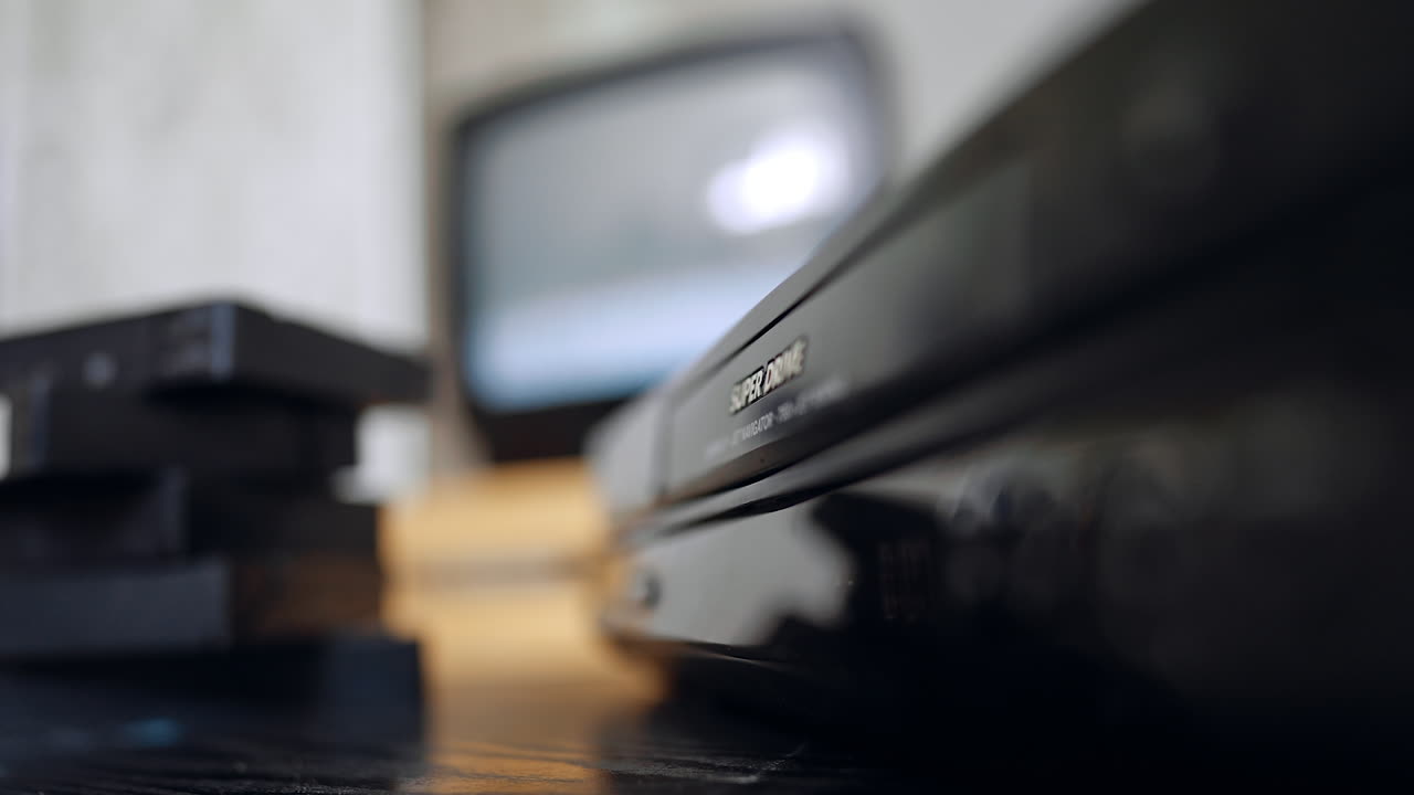 Blurred image of a DVD player, pile of tapes and old TV screen. Close up. Hand presses the buttons