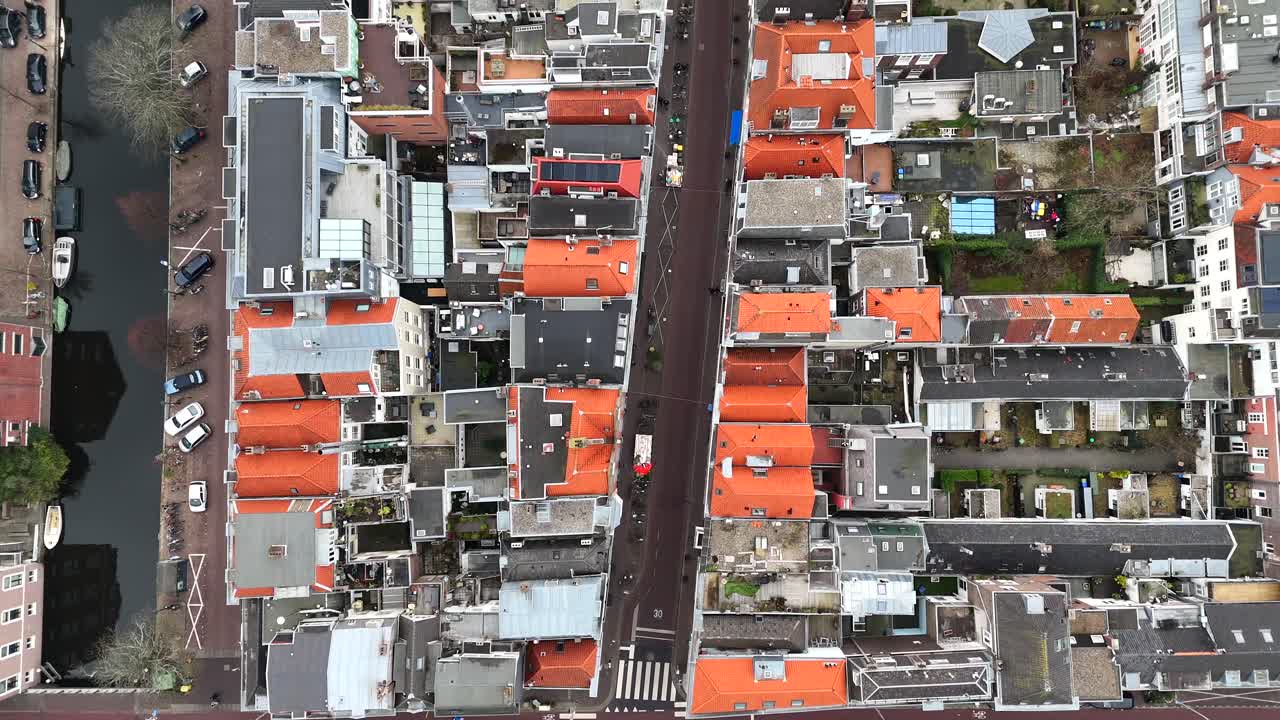 Canals between dense populated housing area with dutch townhouses in The Hague Town. Aerial top down flyover shot. Car on street in city. Cold winter with residential area.