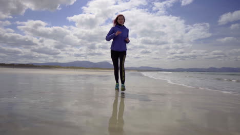 Low-Dolly-Shot-Eines-Mädchens,-Das-An-Einem-Wunderschönen-Sonnigen-Tag-In-Irland-In-4k-Am-Ufer-Eines-Sandstrandes-Mit-Atlantikwellen-Joggt