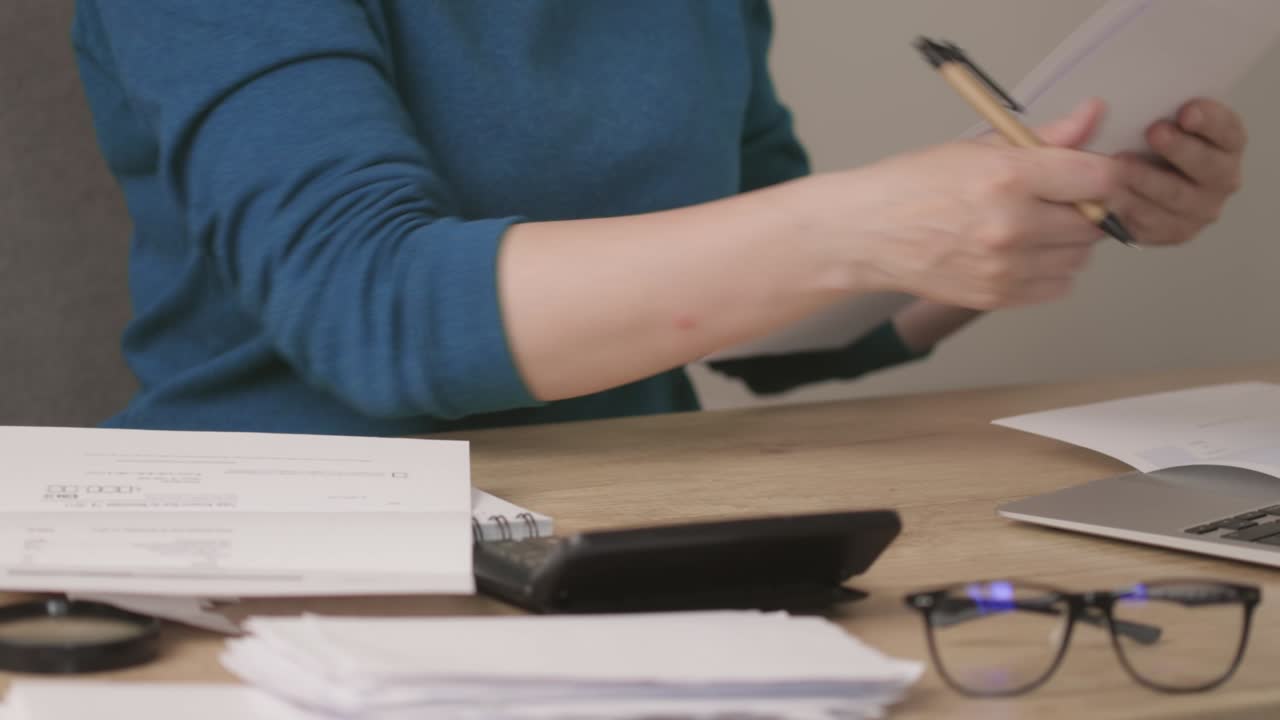 Mani di donna in camicia blu che esaminano documenti cartacei e bollette delle utenze