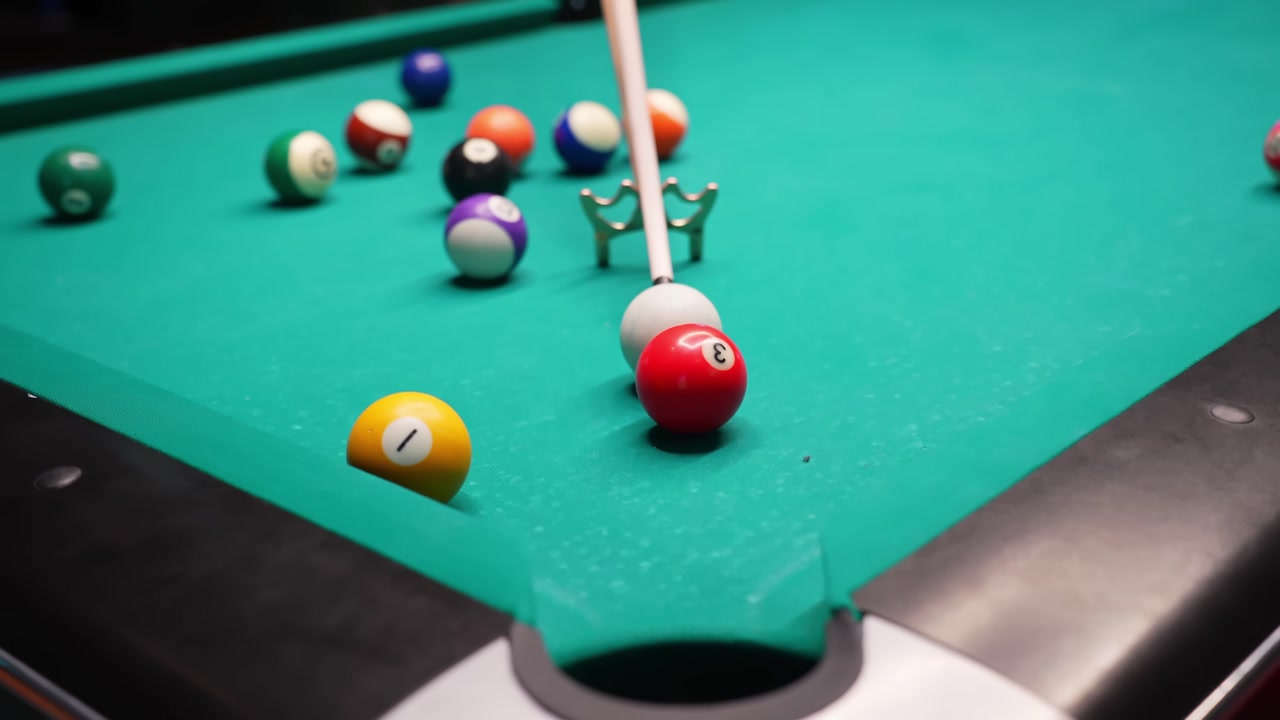 Pool table close-up as a cue aims at the red 3 and it drops into a pocket, with scattered solids and stripes on green felt in a cinematic pub game scene.