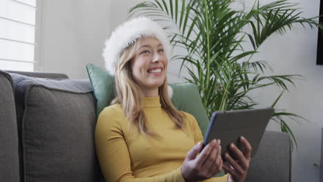 Happy-biracial-woman-wearing-santa-hat-using-tablet-for-christmas-video-call,-in-slow-motion