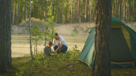 fasten pegs in the ground to assemble a tent in the forest on the lake. family vacation in nature. a boy of 3 years and a man's father together on a hike put a tent.