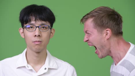 분노한 젊은 스칸디나비아 사업가가 젊은 아시아 사업가에게 비명을 지르고 있다.