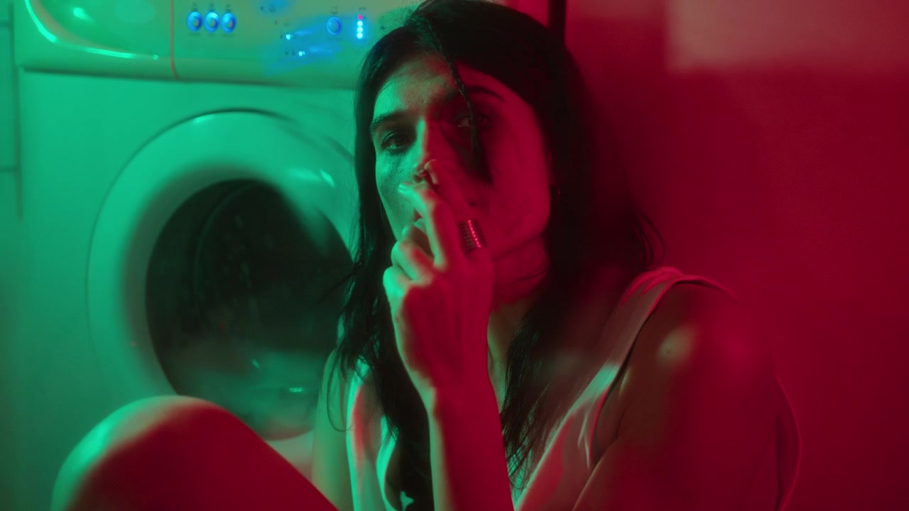 Donna triste con mascara sbavato che fuma in lavanderia con luce al neon