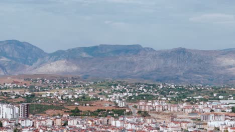 Panoramic-aerial-view-across-Side-South-eastern-mountain-range-and-red-tiled-resort-town-rooftops,-Turkey