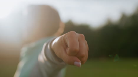 close up of coach wearing ash and mint tracksuit performing forearms curls exercise during sunset on open green field with bright natural sunlight filtering through peaceful outdoor environment