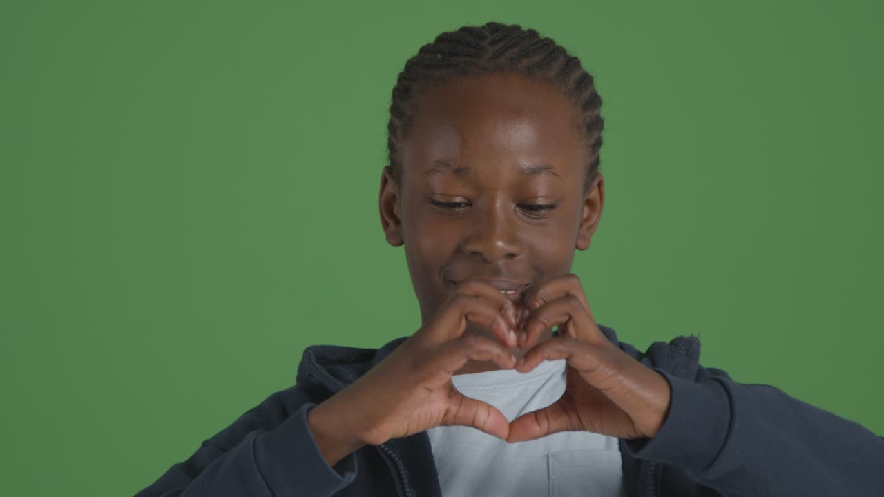 retrato de estudio de niño haciendo forma de corazón con las manos contra el fondo verde