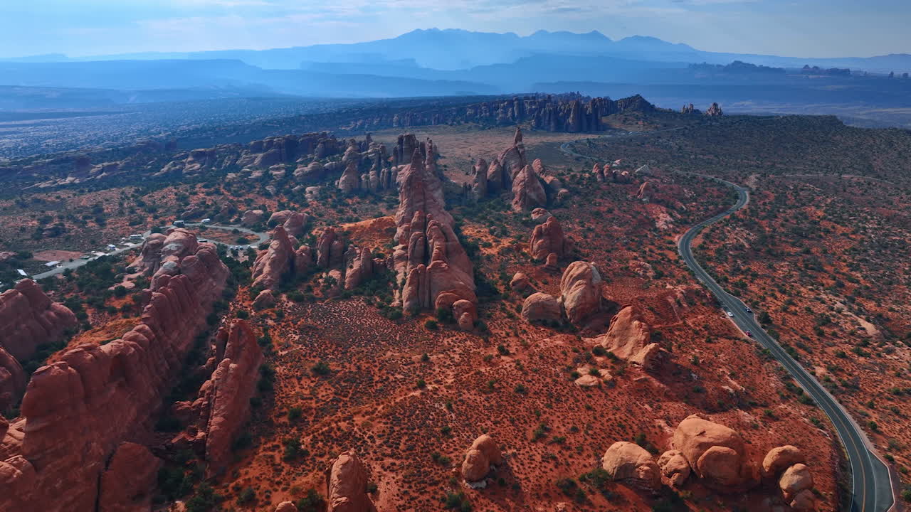 Paesaggio mozzafiato delle rocce arrotondate nel deserto, ricoperte di arbusti. Auto percorrono l'autostrada lungo i canyon. Il Parco nazionale degli Arches nello Utah, USA. Vista aerea