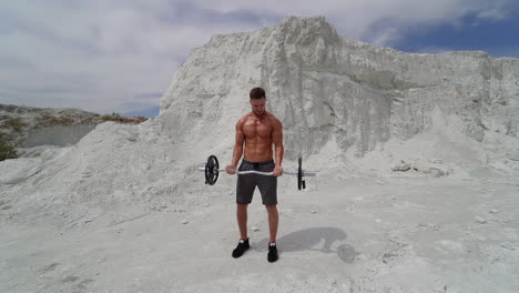 man training in the mountain. outdoor shot of sportsman in training wear, standing on mountain top with barbell