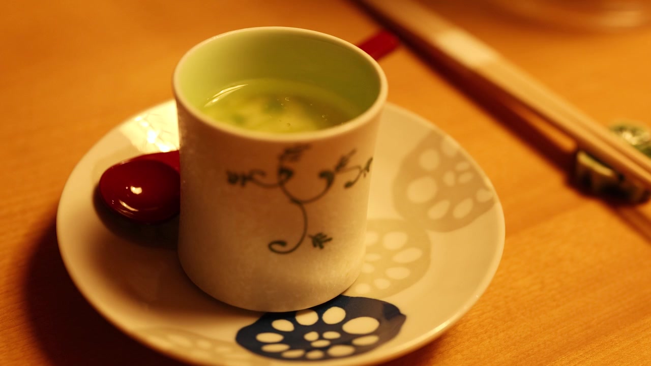 温かい日本の茶碗蒸しが入った陶器のカップから、手が蓋を持ち上げている。