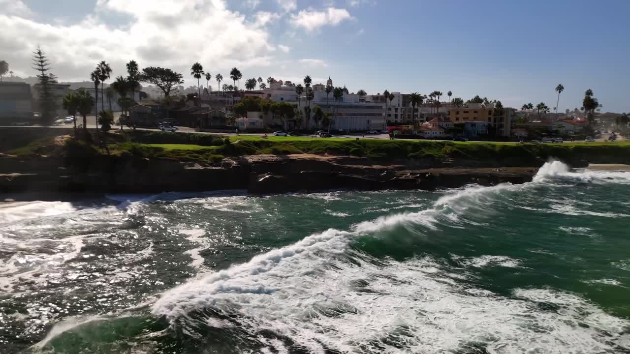 A bright overhead drone shot of La Jolla Cove’s rugged cliffs and crystal-blue shoreline under clear midday light