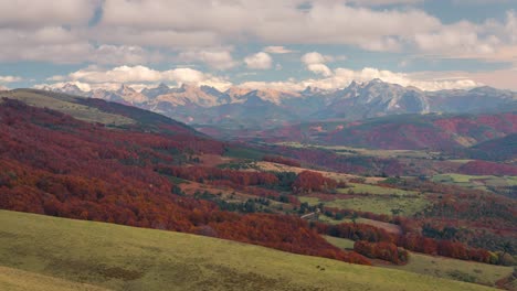 timelapse view of snowy mountain peaks, orange and green forest in fall autumn season on a sunny and cloudy day