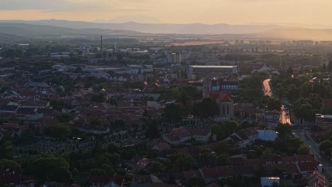 An aerial video of a historic European town at sunset, featuring a prominent church in the foreground and a winding road leading into the distance. The soft golden light highlights the rooftops