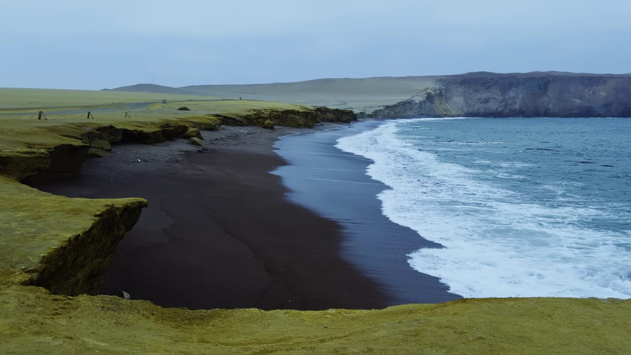 Long wave crashes along Playa de Rojas shoreline with scenic coastal terrain visible, slow motion establishing static