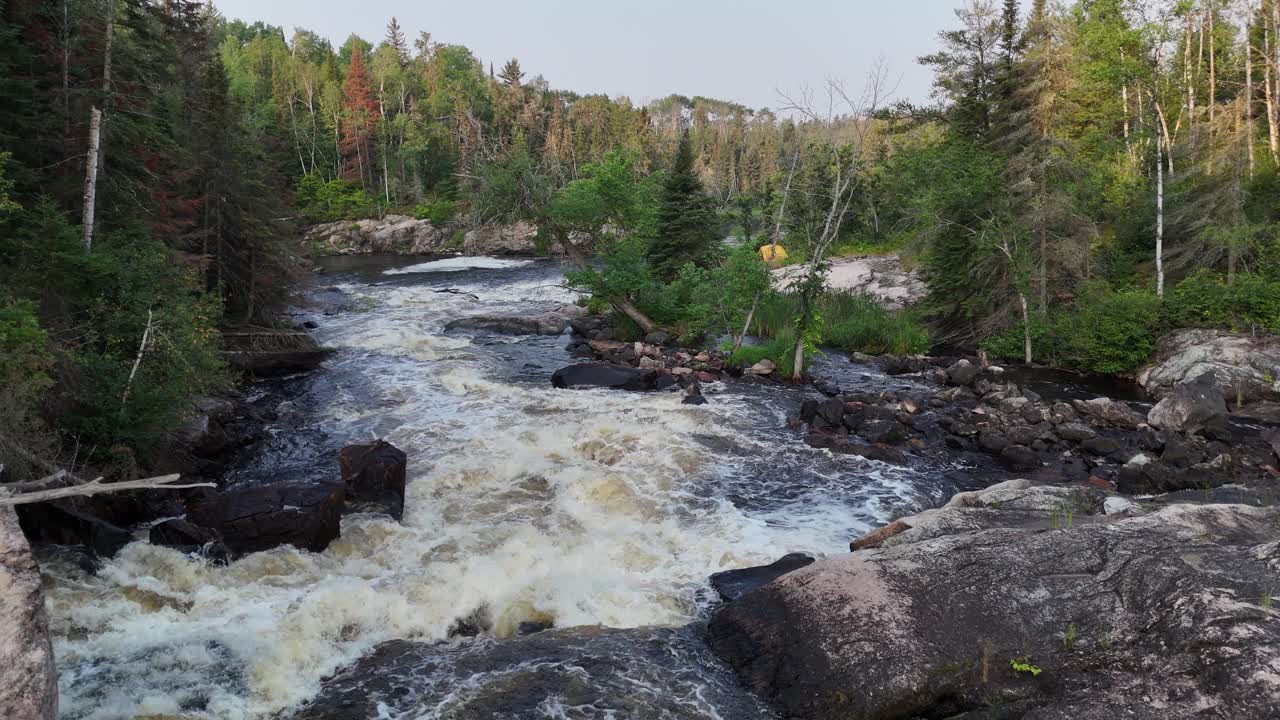 Turtle Falls on the Manigotagan River in Manitoba flowing over Canadian Shield granite. The aerial camera flies low downstream along fast rapids through the summer boreal forest