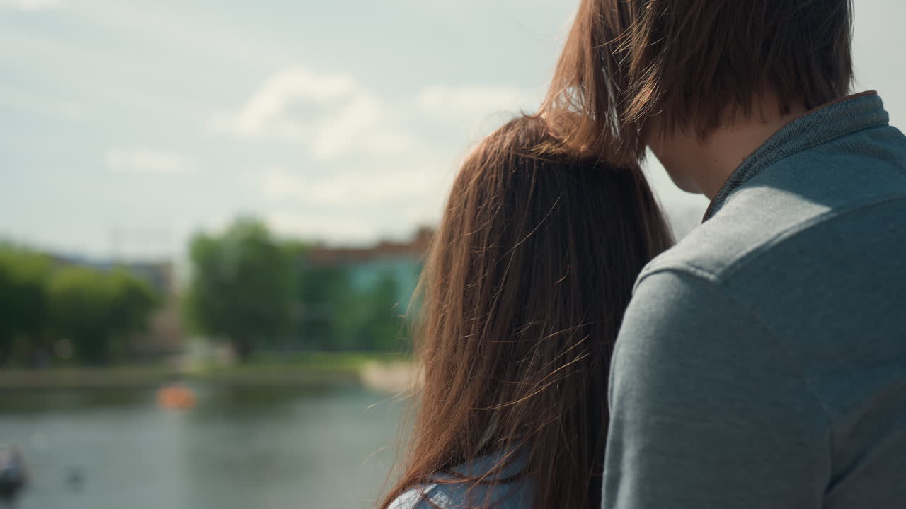 강가에서 포옹하는 백인 커플, 물에 비치는 부드러운 스카이라인, 뒤에서 클로즈업, 조용한 여름 오후, 부드러운 속삭임, 물가의 산책로, 잔잔한 바람, 낭만적인 사색, 도시