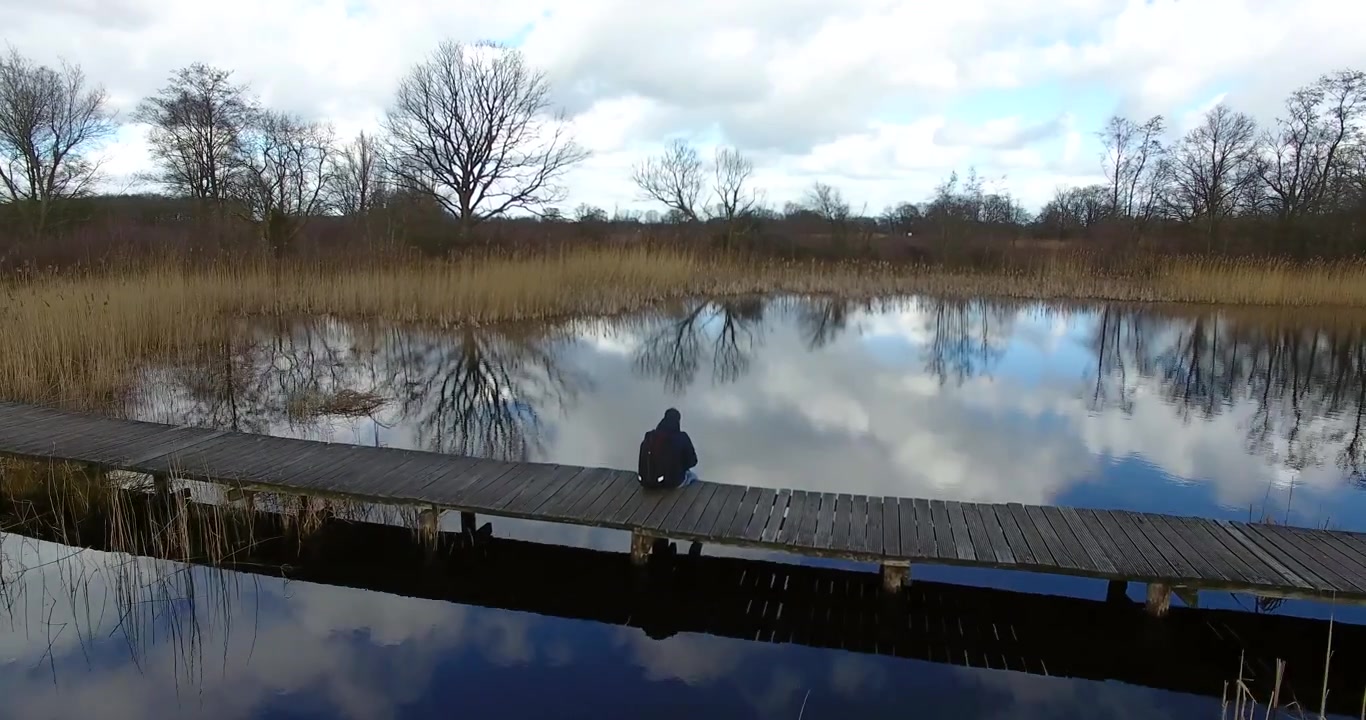 Aerial shot of a guy sitting alone on a small wooden bridge on a lake in Holland in the winter.