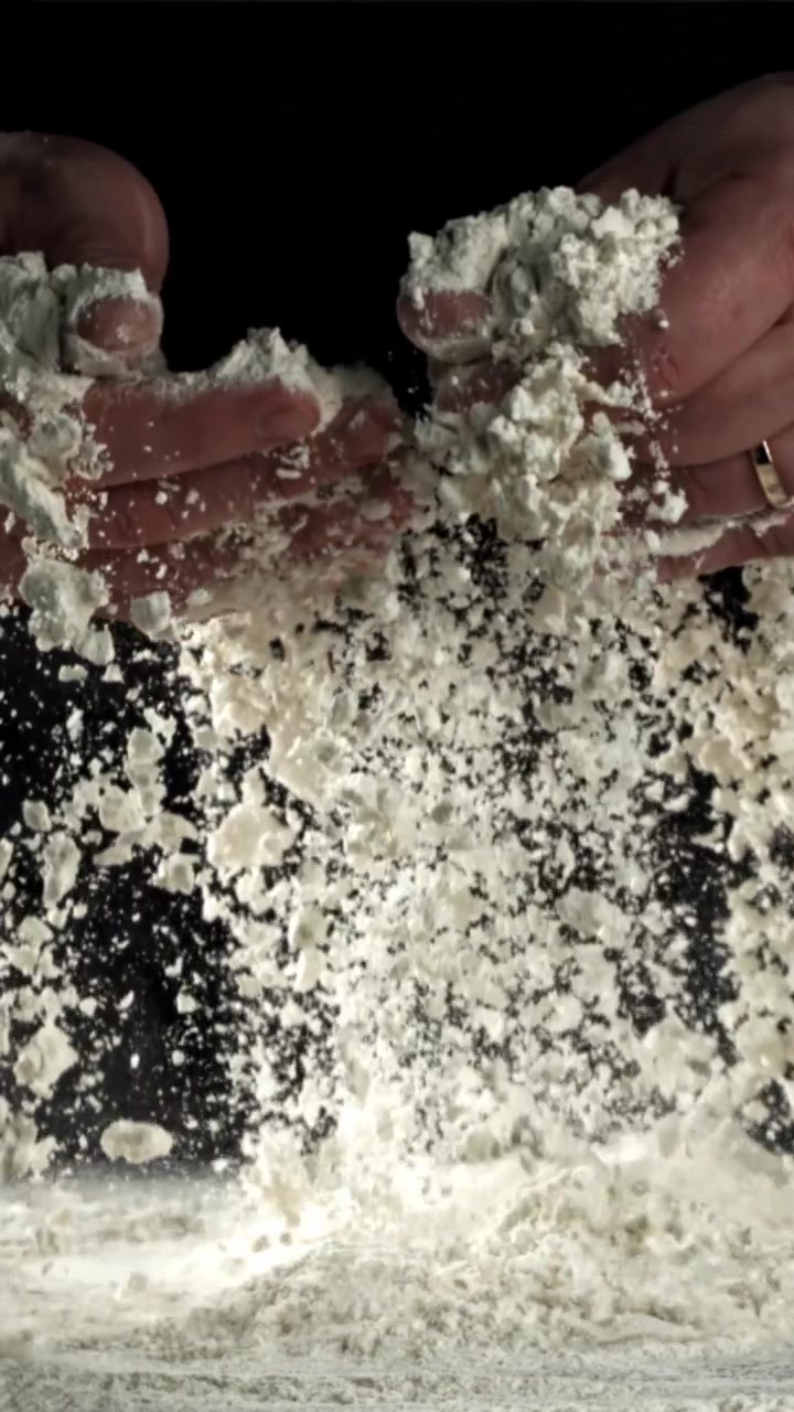 Hænder sigter hvidt mel i slowmotion