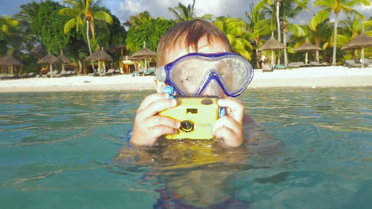 niño bañándose en el océano y tomando fotos con una cámara impermeable