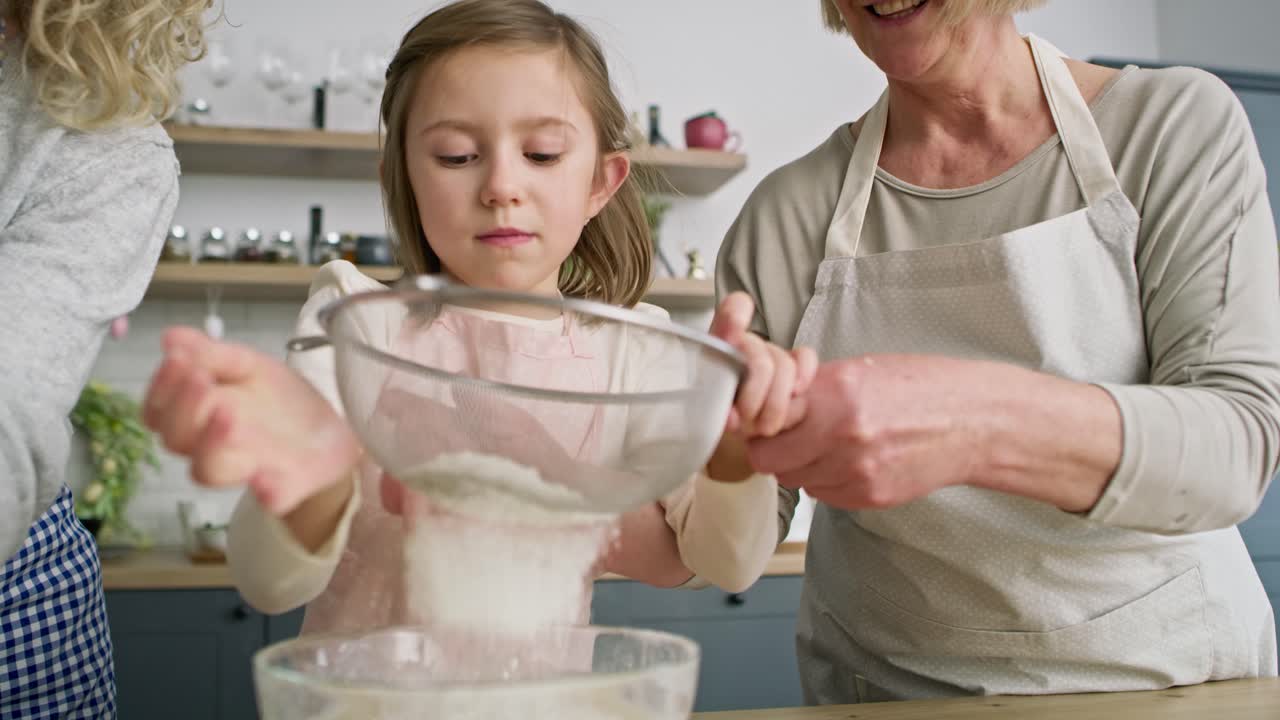 Handheld video of girl with mother and grandmother sifting flour