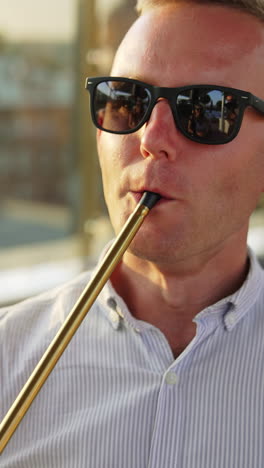 mid aged man in sunglasses holding shisha pipe in his mouth. close up. relaxed man in shirt smoking hookah in the café outdoors. vertical video