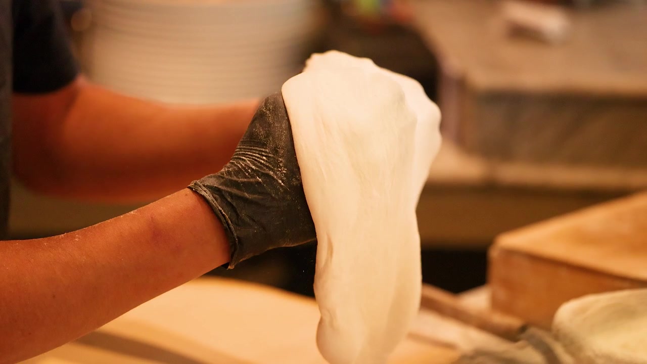 Close-up of chef stretching fresh dough by hand in a warm restaurant kitchen setting.