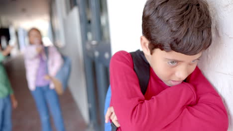 in school, young biracial boy with dark hair leaning against a wall, being bullied